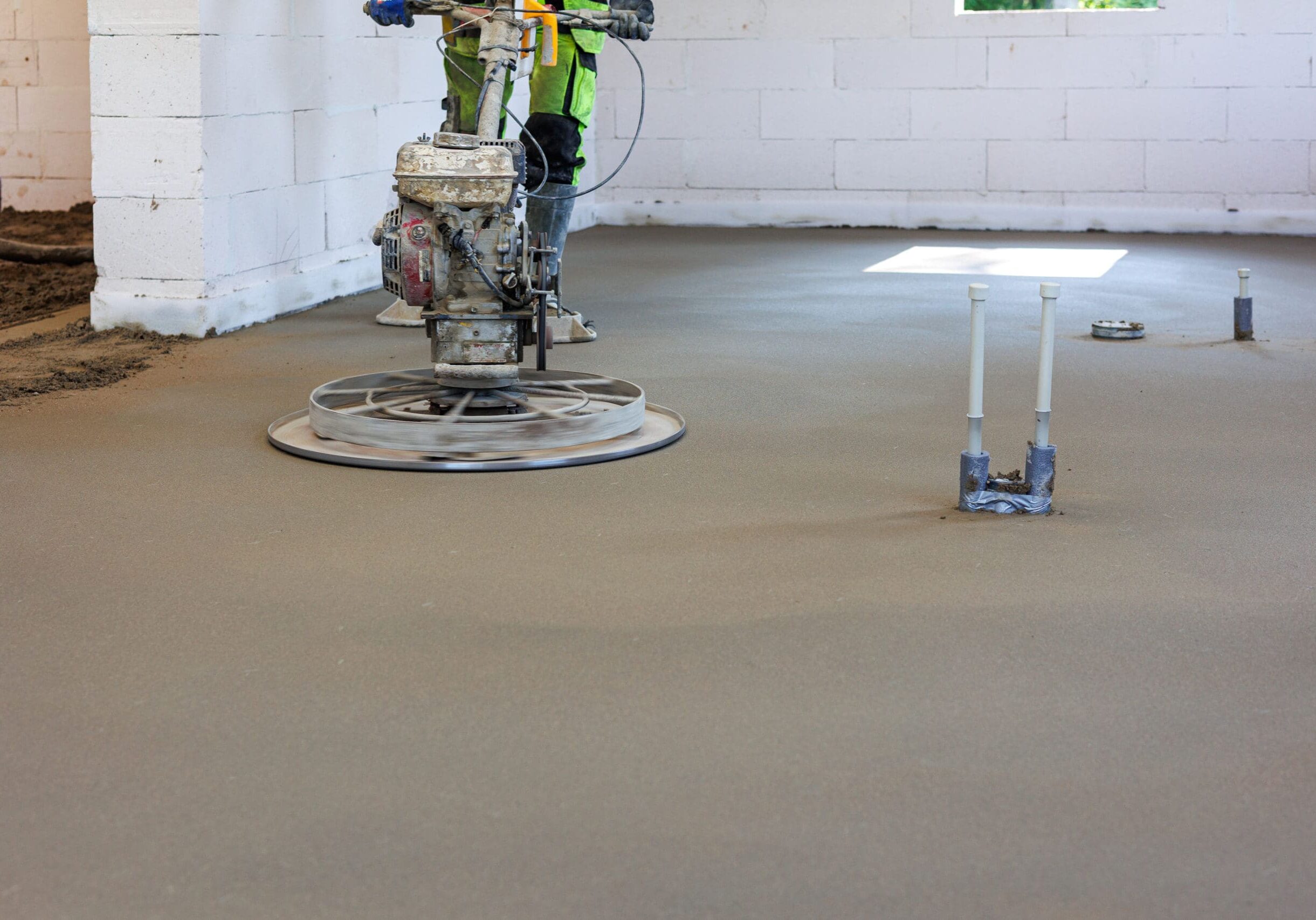 Concrete Floor Smoothing with Power Trowel in New Building, Worker using power trowel machine to smooth freshly poured concrete floor during interior construction of a modern residential house.